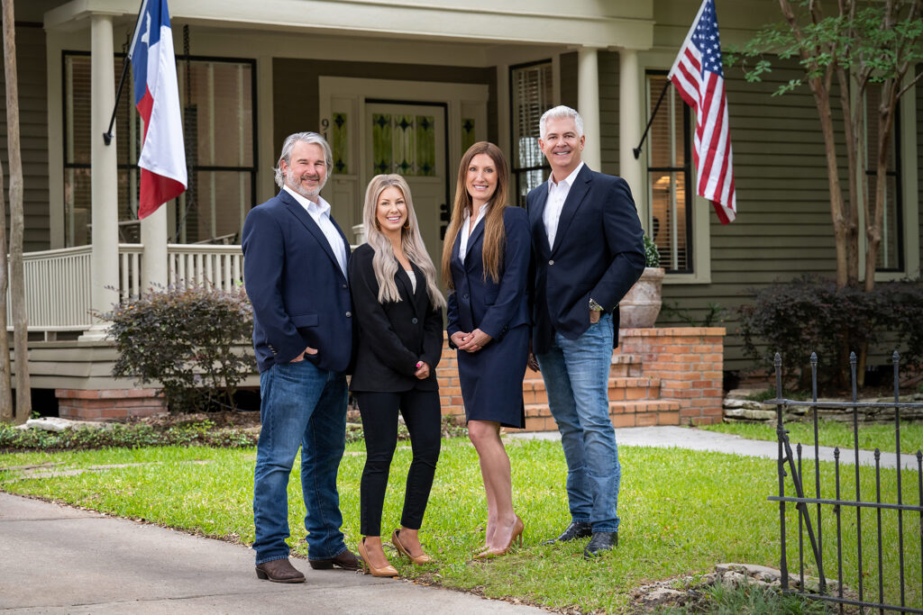Group portrait of four professionals standing outdoors in front of a house with U.S. and Texas flags.
