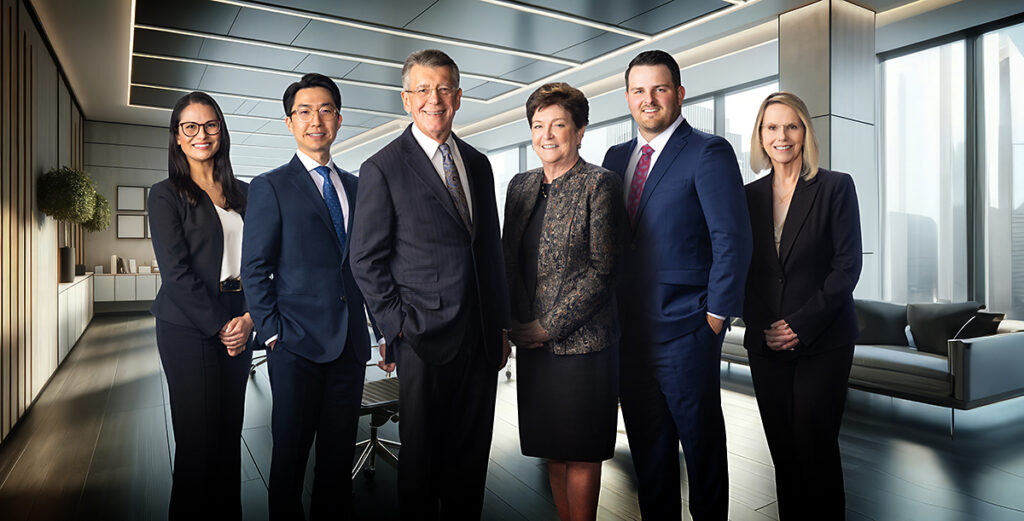 Composite executive team portrait of six professionals in business attire standing together in a modern office setting.