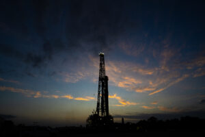 Silhouette of a Texas drilling platform at sunset with tower lights visible, photographed for a safety report. Escape cable and structural cables included for operational accuracy. Enhanced sky colors and contrast for visual impact. Photographed by Solaris Studios.