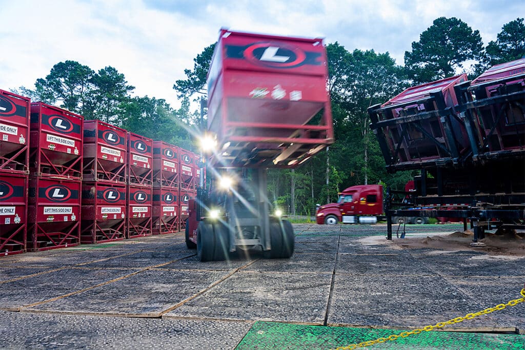 Industrial site in northeast Texas with forklift moving left to right framing a semi-truck moving right to left, shot with slow shutter speed to capture motion blur, bold red equipment, and security chain in foreground, photographed by Solaris Studios.