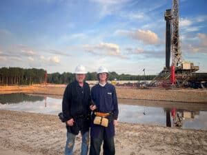 Photographer Aric with his son Gavin on a Texas oil and gas drilling site, wearing hard hats at sunset. Photographed on an iPhone by a security escort during a three-day industrial photography assignment.