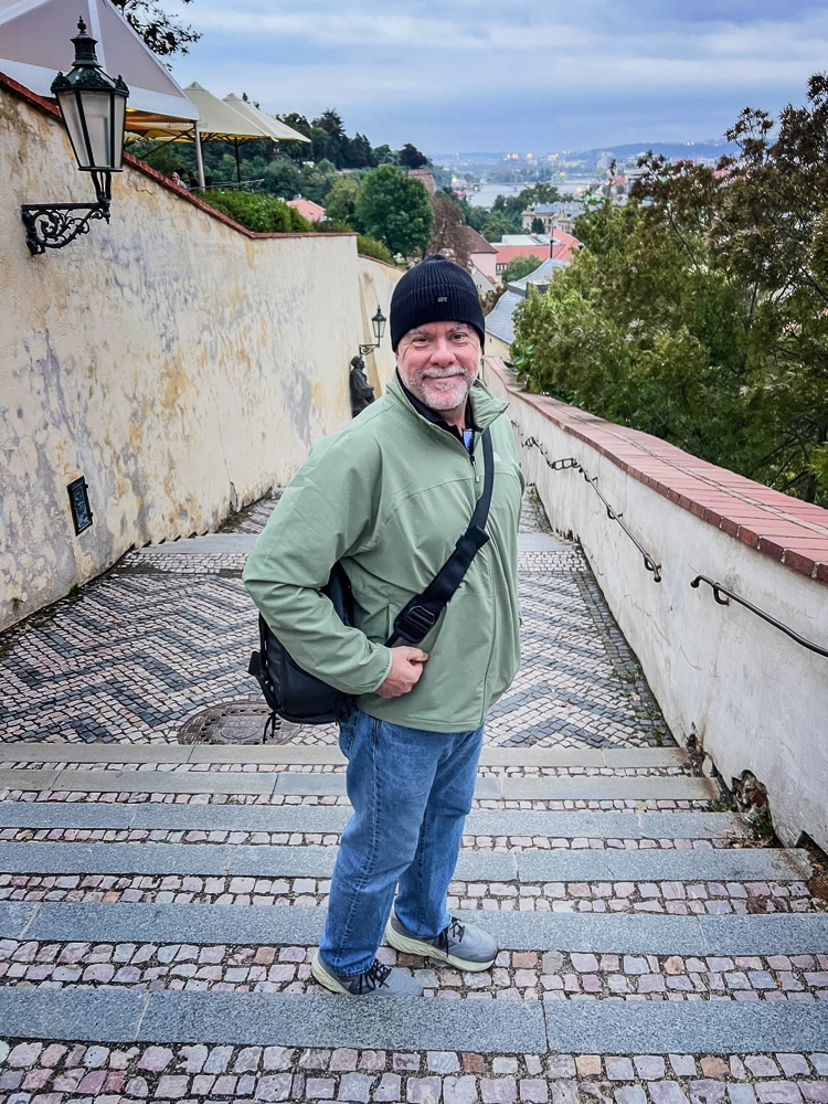 Photographer standing with the Bevis Gear camera bag slung crossbody, midway up a staircase in Prague en route to the castle, overlooking the city in the early morning light.
