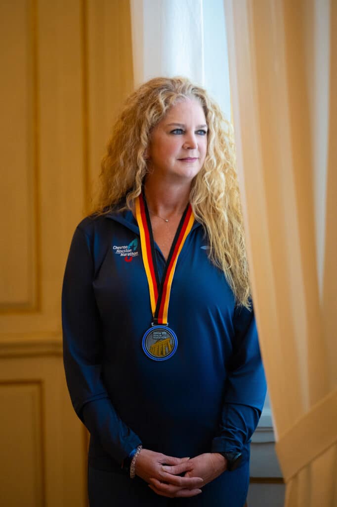 Portrait of Toni standing near a window inside Nymphenburg Palace, wearing her Berlin Marathon 2025 medal. Photographed in soft natural light, this image captures the quiet pride and accomplishment following her marathon finish in Berlin.