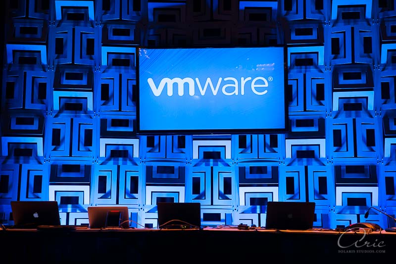 VMware branded conference stage setup with laptops, presentation screen, and blue event lighting before a corporate technology presentation