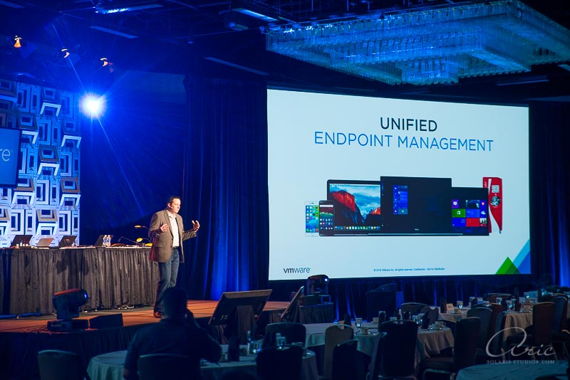 Keynote speaker presenting VMware unified endpoint management on a large conference screen during a corporate technology event