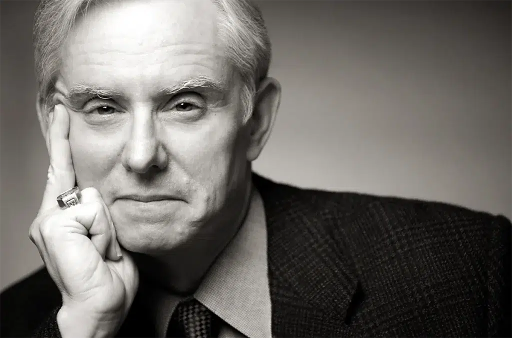 Black-and-white close-up portrait of an older man resting his face on his hand, wearing a suit and tie.