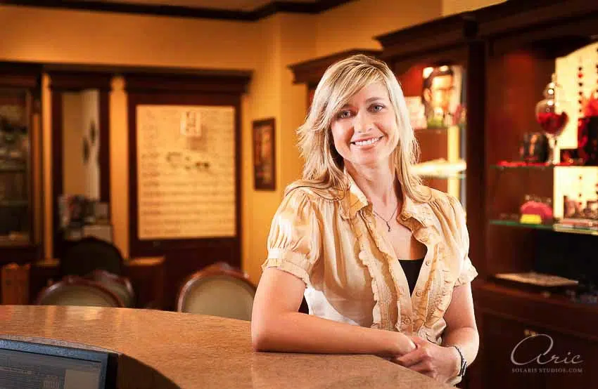 Environmental professional headshot of hospitality business owner at reception desk photographed with warm interior lighting and shallow depth of field for executive branding