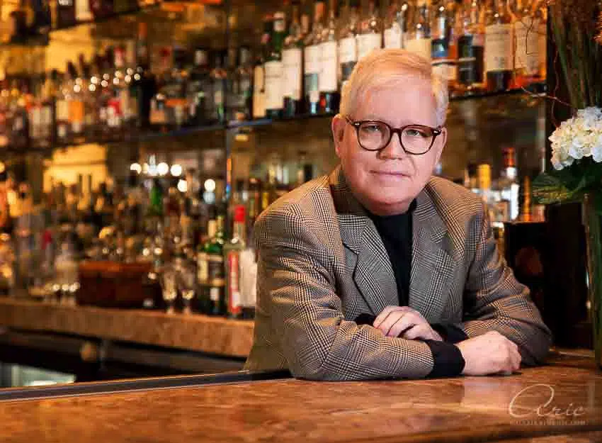 Environmental executive portrait of bar owner at upscale cocktail lounge photographed with warm ambient bar lighting and shallow depth of field for hospitality leadership branding