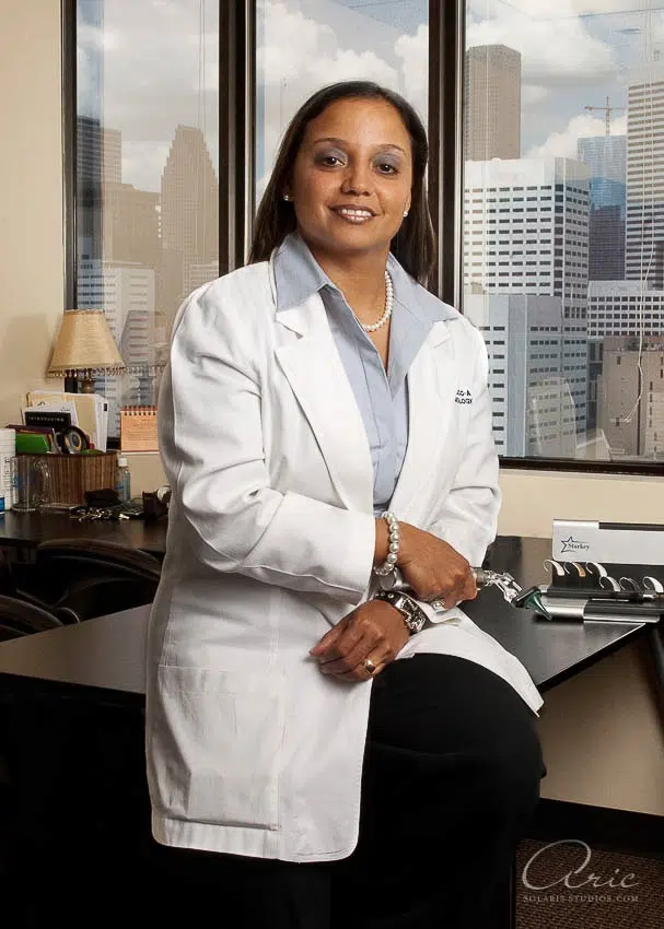 Environmental professional headshot of medical doctor in office with city skyline background photographed with soft window lighting and shallow depth of field for professional healthcare profile