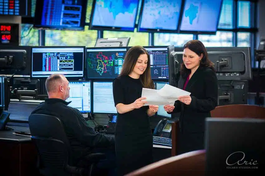 Corporate operations team portrait of professionals reviewing reports in technology control room photographed with balanced office lighting and wide environmental composition