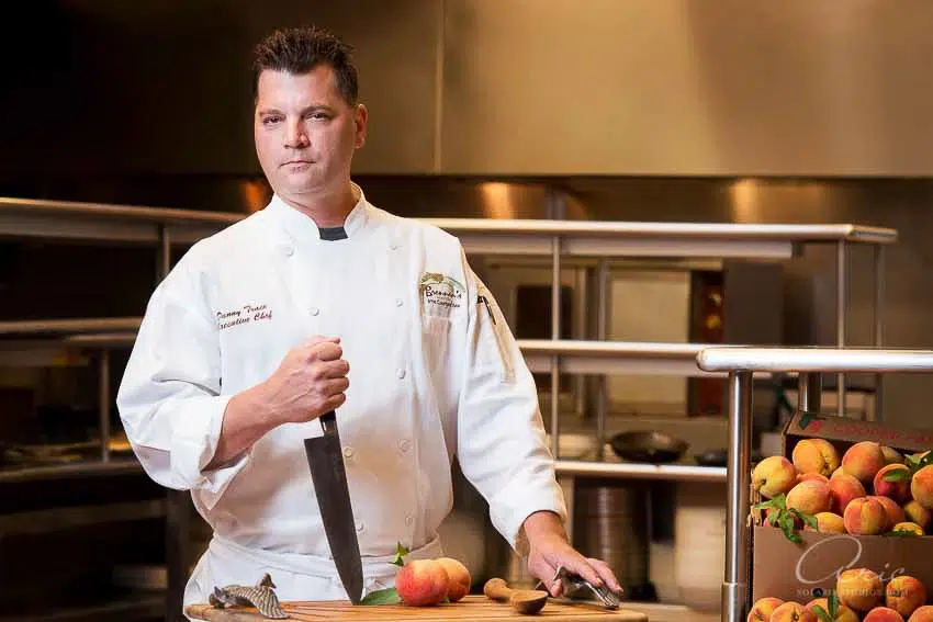 Environmental executive portrait of professional chef preparing fresh ingredients in commercial kitchen photographed with soft directional lighting and shallow depth of field for culinary leadership branding