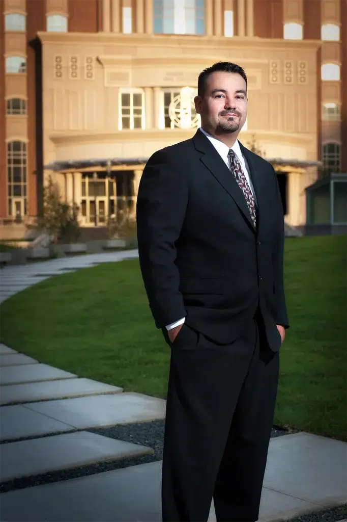 Environmental executive portrait of business professional photographed outdoors in front of corporate office building using balanced off-camera lighting and architectural background for leadership branding