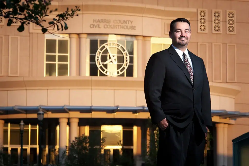 Man in a suit standing outdoors in front of the Harris County Civil Courthouse building with a clock visible behind him.
