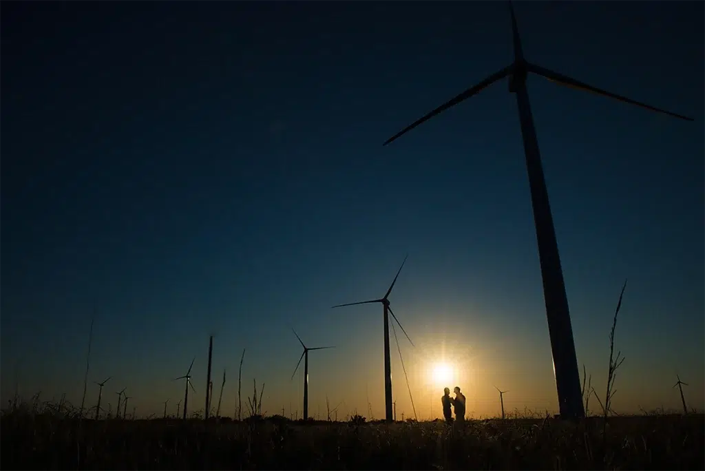Environmental corporate portrait silhouette of renewable energy professionals at wind farm during sunset photographed with dramatic backlighting and expansive landscape composition