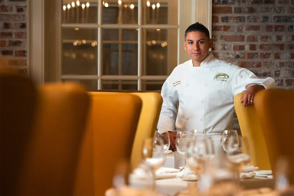 Environmental professional headshot of executive chef standing in upscale restaurant dining room photographed with soft directional lighting and shallow depth of field for personal branding