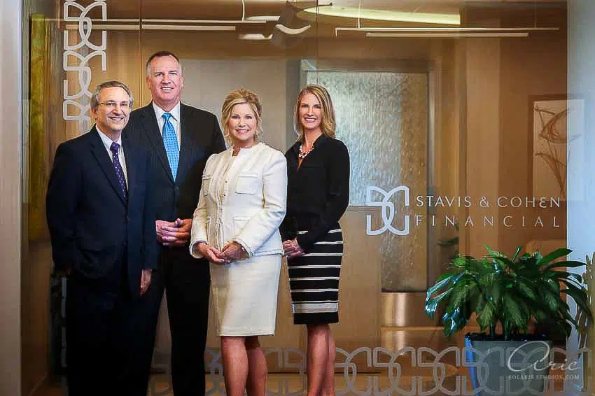 Group portrait of four executives in business attire standing in an office lobby behind glass with the company name displayed.