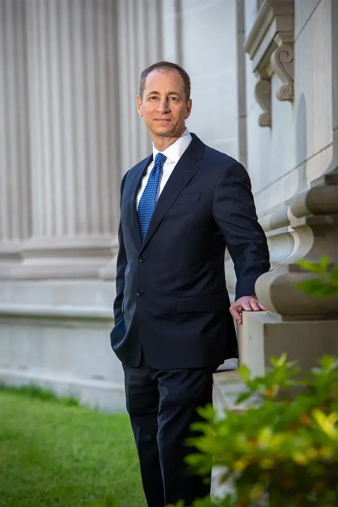 Executive in a dark suit and blue tie standing outdoors near a stone building with large columns.