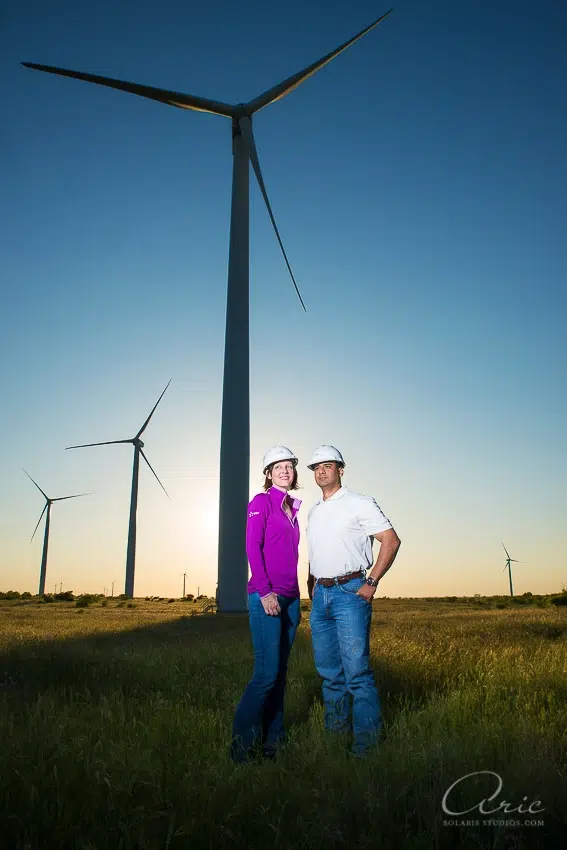 Environmental corporate portrait of renewable energy professionals standing beneath wind turbines photographed with dramatic natural light and wide-angle landscape composition for industry leadership branding