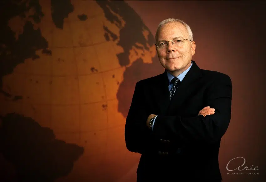 Professional executive headshot of corporate leader photographed with directional studio lighting and global map background for corporate leadership profile portrait