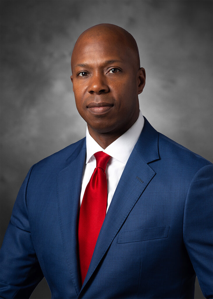 Executive corporate headshot after professional retouching with refined skin tone, subtle facial smoothing, and enhanced background for a polished portrait