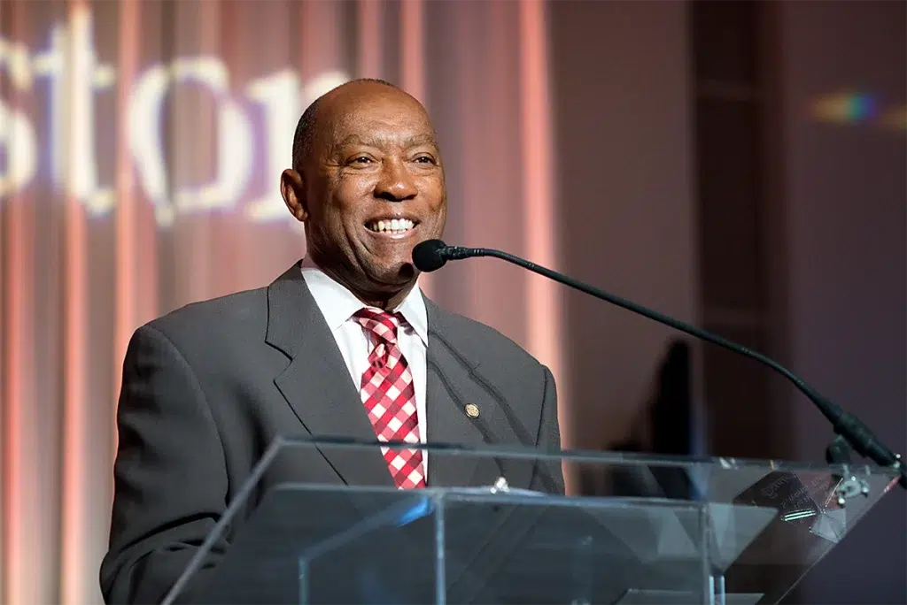 Former Houston Mayor Sylvester Turner delivering a keynote speech at a event while speaking at a podium under stage lighting