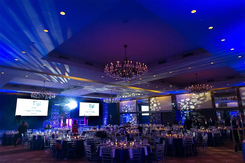 Elegant corporate gala ballroom setup with stage lighting, projection screens, and round banquet tables prepared for a formal awards event