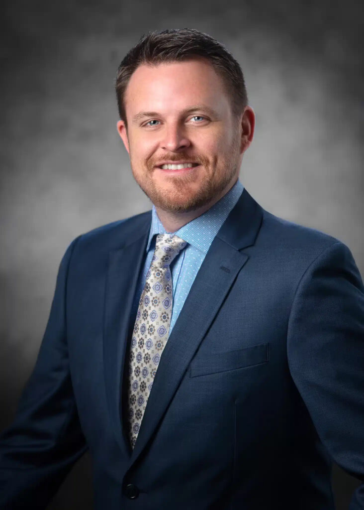 Professional corporate headshot of male executive photographed with soft studio lighting and neutral gray gradient background for business profile and LinkedIn branding
