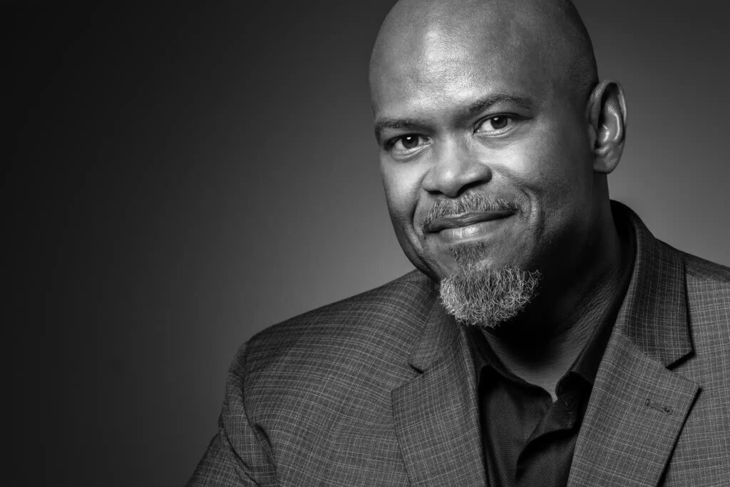 Black and white studio headshot of business executive photographed with dramatic directional lighting and neutral gradient background for professional corporate branding