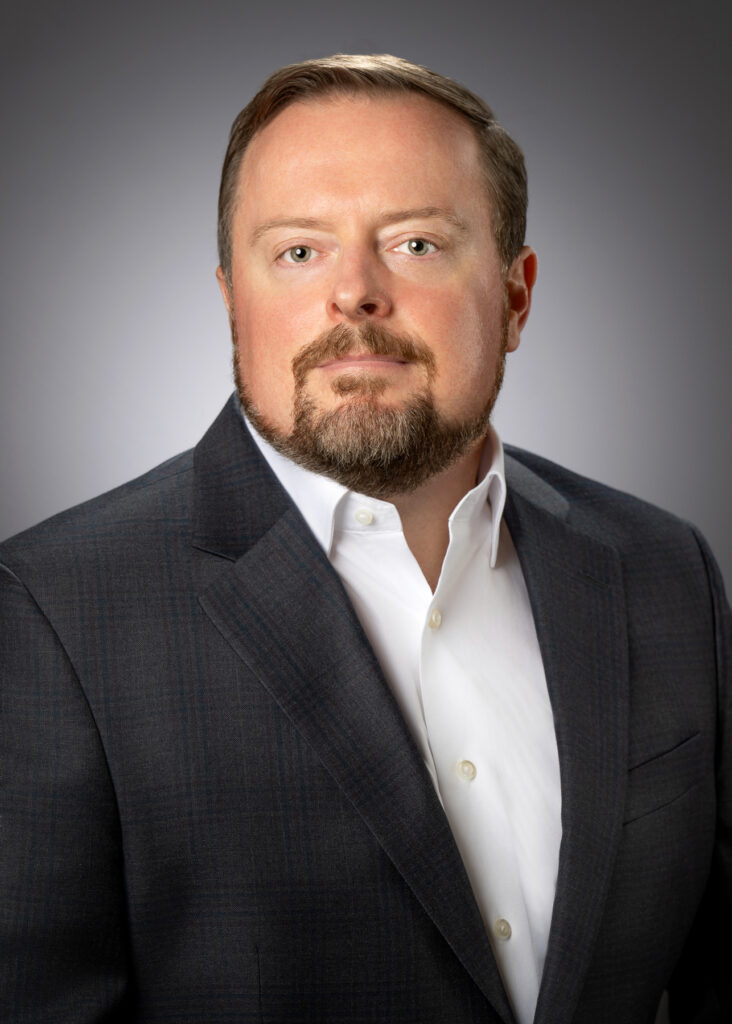 Professional studio headshot of male executive in patterned suit jacket photographed with soft studio lighting and neutral gray background for corporate branding and LinkedIn profile. For Headshot Photography Portfolio