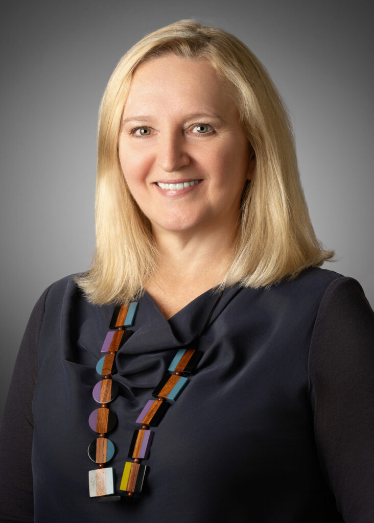Professional studio headshot of female executive wearing statement necklace photographed with soft studio lighting and neutral gray background for corporate branding and LinkedIn profile. For Headshot Photography Portfolio