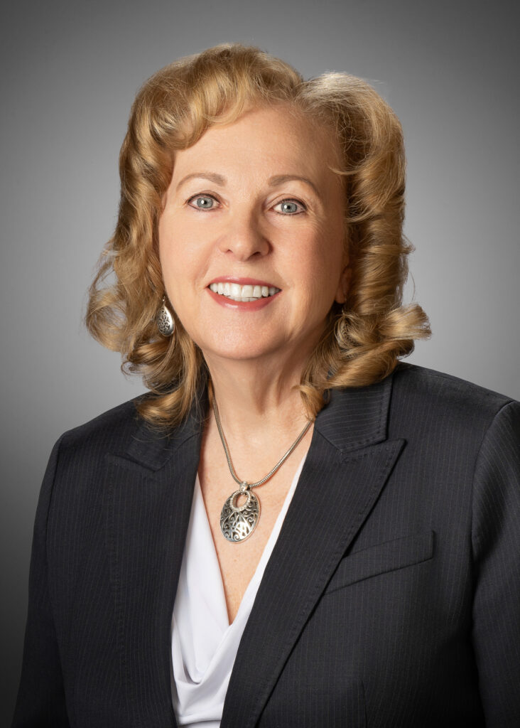 Professional studio headshot of female executive wearing dark blazer and silver pendant necklace photographed with soft studio lighting and neutral gray background for corporate branding and LinkedIn profile. For Headshot Photography Portfolio