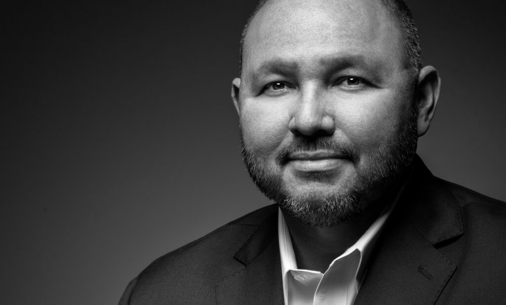 Black and white studio headshot of male executive photographed with dramatic directional lighting and dark gradient background for professional corporate branding
