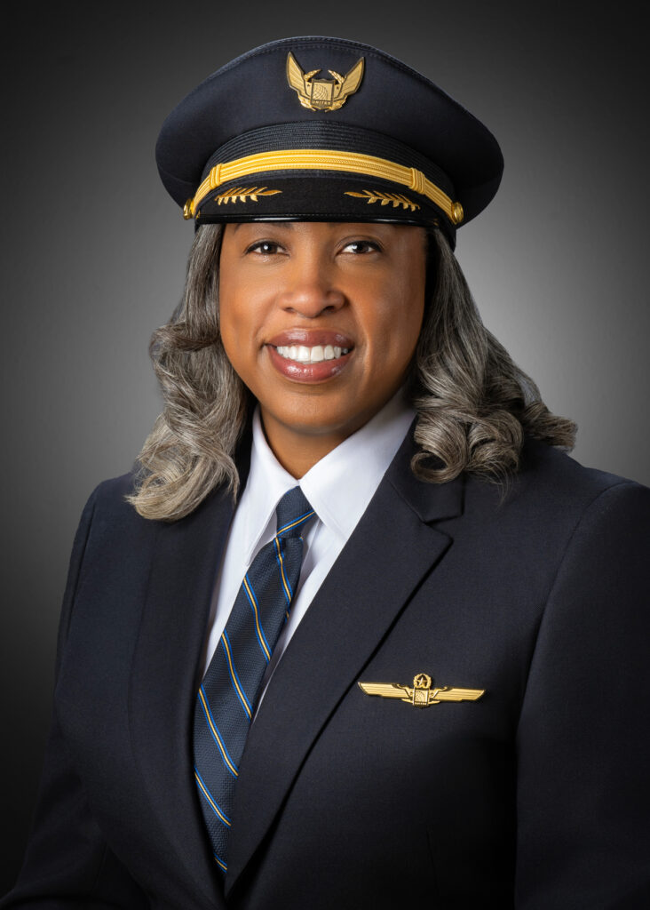 Professional studio headshot of female airline pilot in uniform photographed with soft studio lighting and dark gray gradient background for corporate branding and executive profile