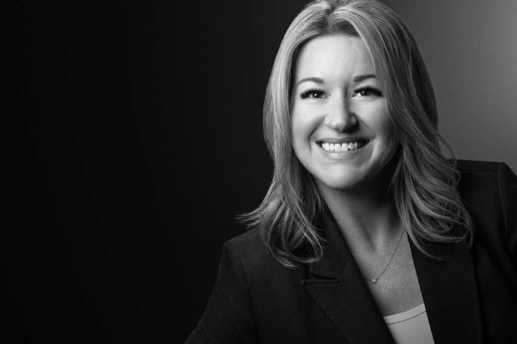 Black and white studio headshot of smiling female executive photographed with dramatic studio lighting and dark gradient background for professional corporate branding. For Headshot Photography Portfolio