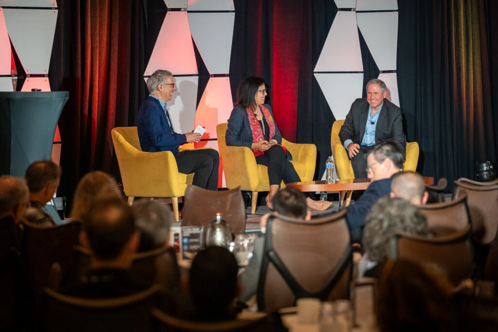 Panel discussion at a critical thinking summit at The Houstonian, with three speakers seated on stage in front of a live audience.