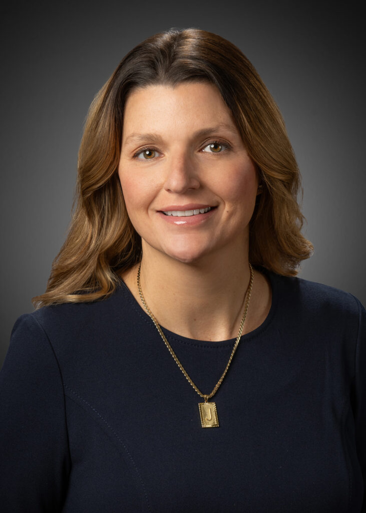 Professional in-studio headshot of a woman in a navy dress against a gray vignette background.