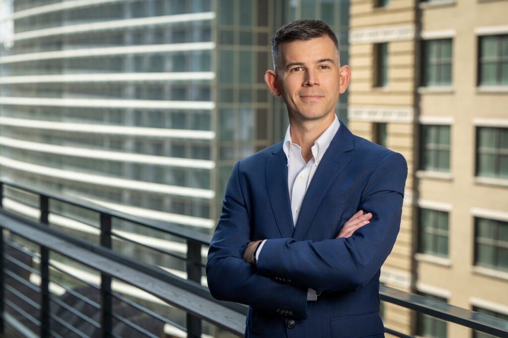 Executive portrait of a businessman on a rooftop in downtown Houston, photographed with balanced sunlight and strobe lighting against an urban background.