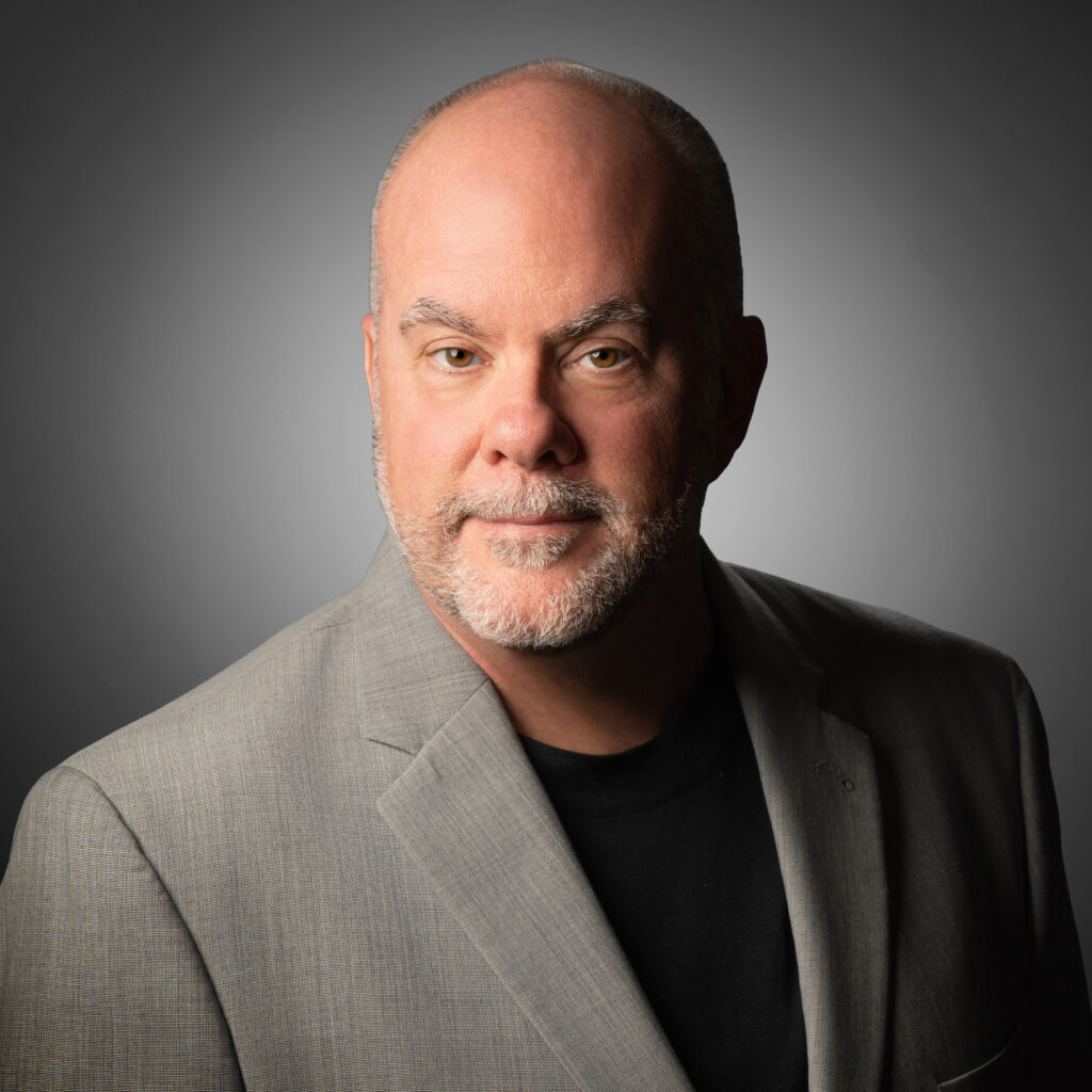 Studio portrait of Aric Hoek in a gray jacket against a gray vignette background.